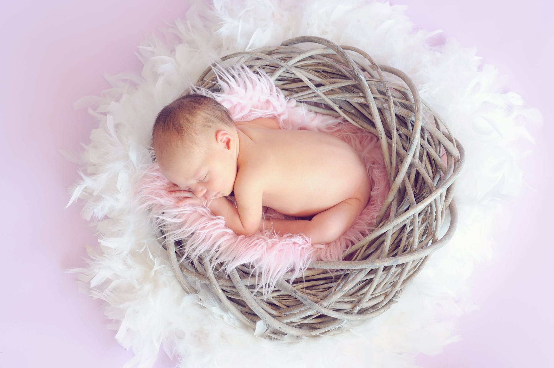 baby sleeping in a basket and a round feather surrounding the basket